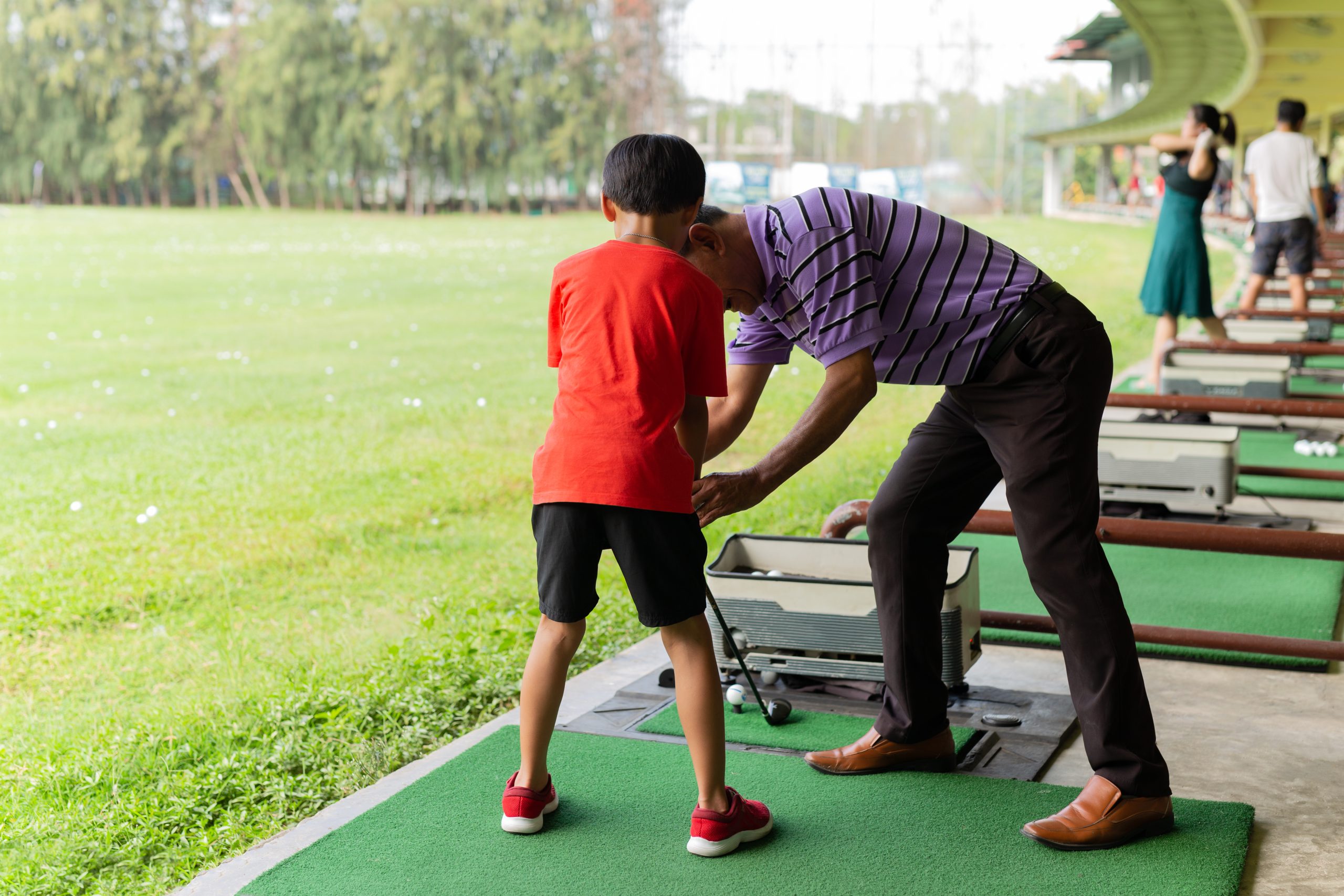 Personal trainer giving lesson to young boy in golf driving range