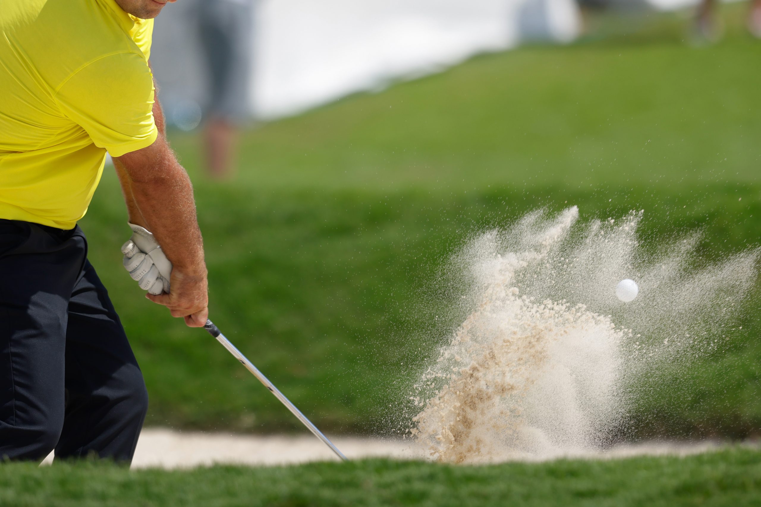 pro golfer hitting a sand bunker shot wearing yellow shirt